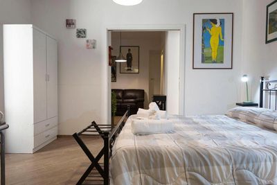 Cozy bedroom with neatly made bed, white wardrobe, and colorful artwork on walls.
