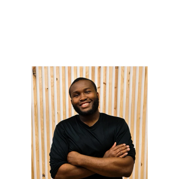 Smiling man with beard and crossed arms stands against a wooden slat wall.