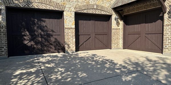 Three dark wooden garage doors painted with rich brown on a stone brick house on the driveway 