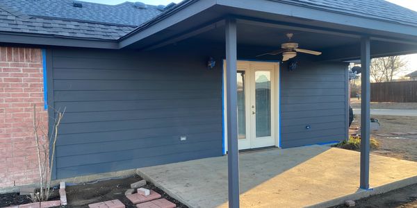 Newly painted blue-gray house exterior with a concrete patio and white French doors.