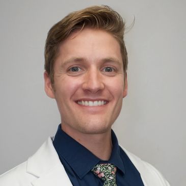 Smiling man in white coat and floral tie.