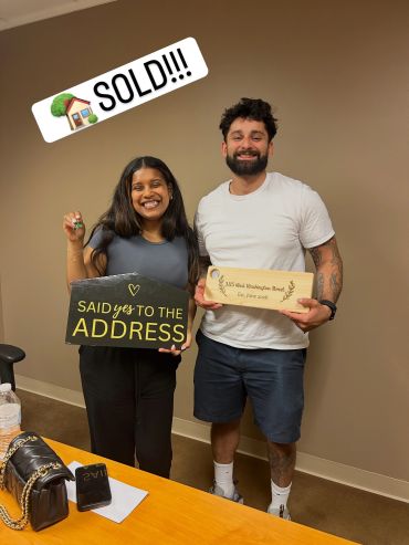 Happy couple celebrating their new home purchase with signs and keys.