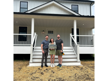 Three people standing in front of a new house holding a welcome sign.