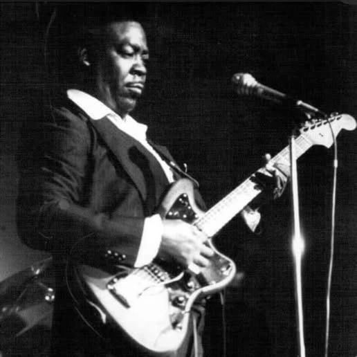 Black and white image of a man playing electric guitar on stage.