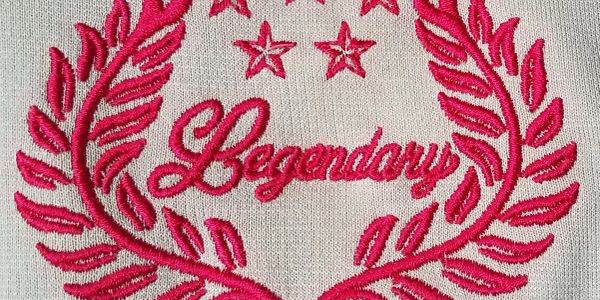 Red embroidered word 'Legendary' with stars and laurel leaves on fabric.