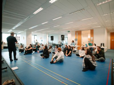 Group attending a presentation in a room with blue flooring.