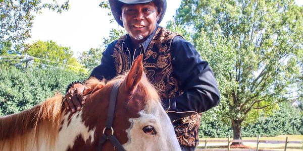 Man in cowboy hat petting a white and brown horse outdoors.