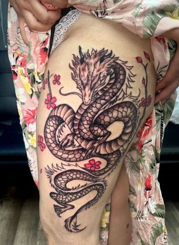 Intricate dragon tattoo with pink flowers on thigh.