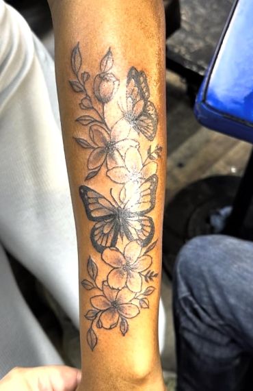 Floral and butterfly black ink tattoo on forearm.