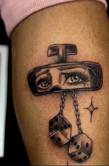 Tattoo of sad eyes in a rearview mirror with dangling dice.