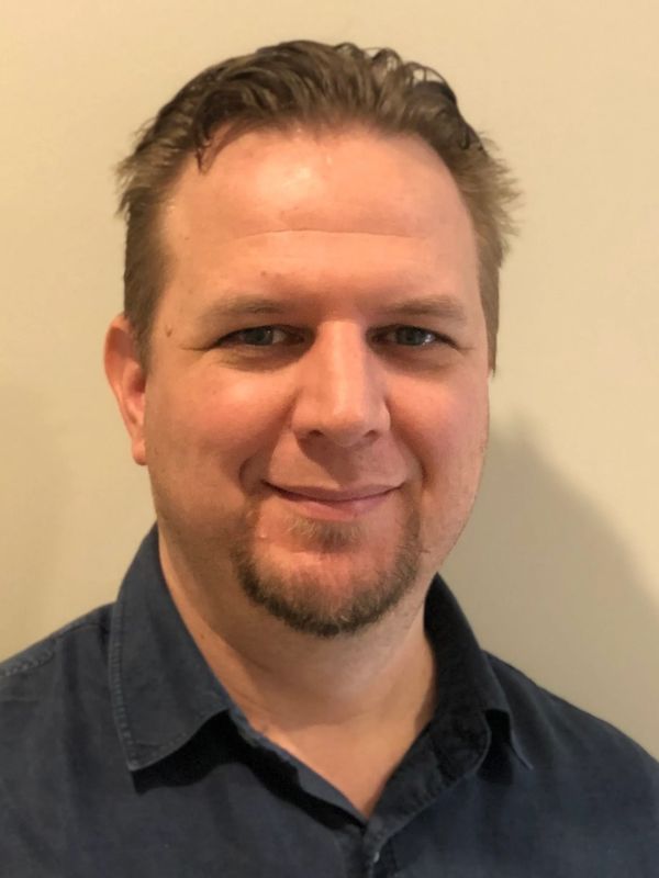 Smiling man with short hair and a goatee wearing a dark blue shirt.