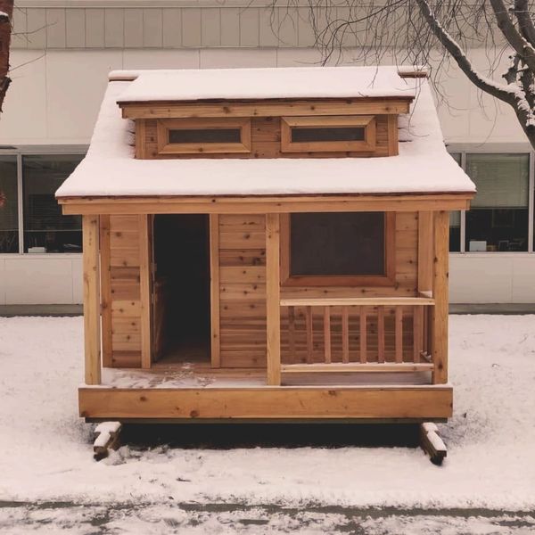 A small wooden cabin covered with snow in a winter setting.