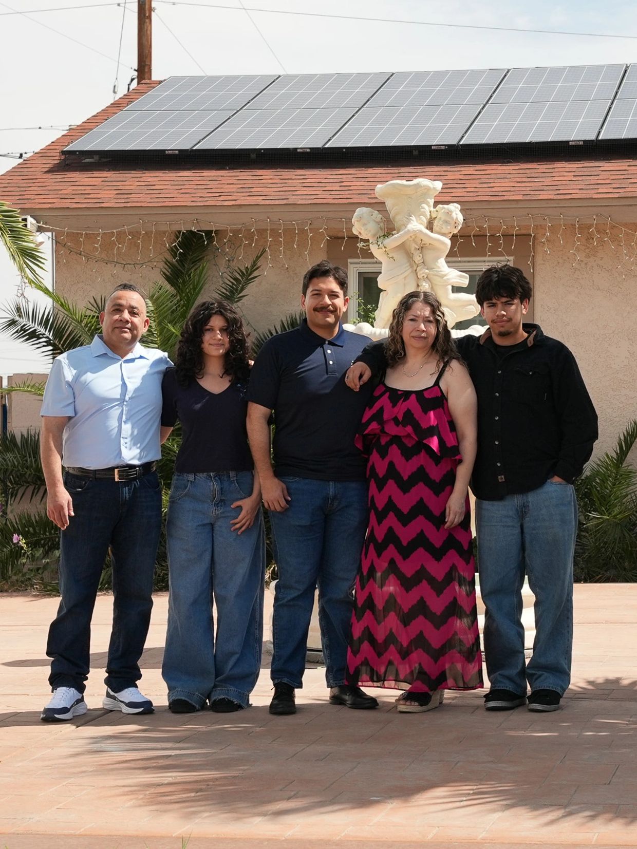 Family of five posing in front of a house with solar panels on the roof.