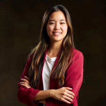 Young woman with long hair in a red jacket smiling.