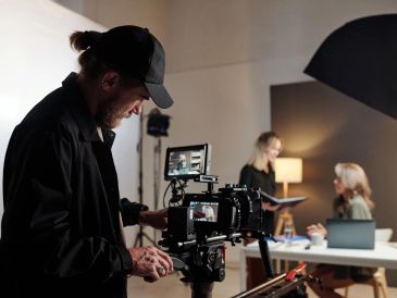 Man operating camera while two women work in background.