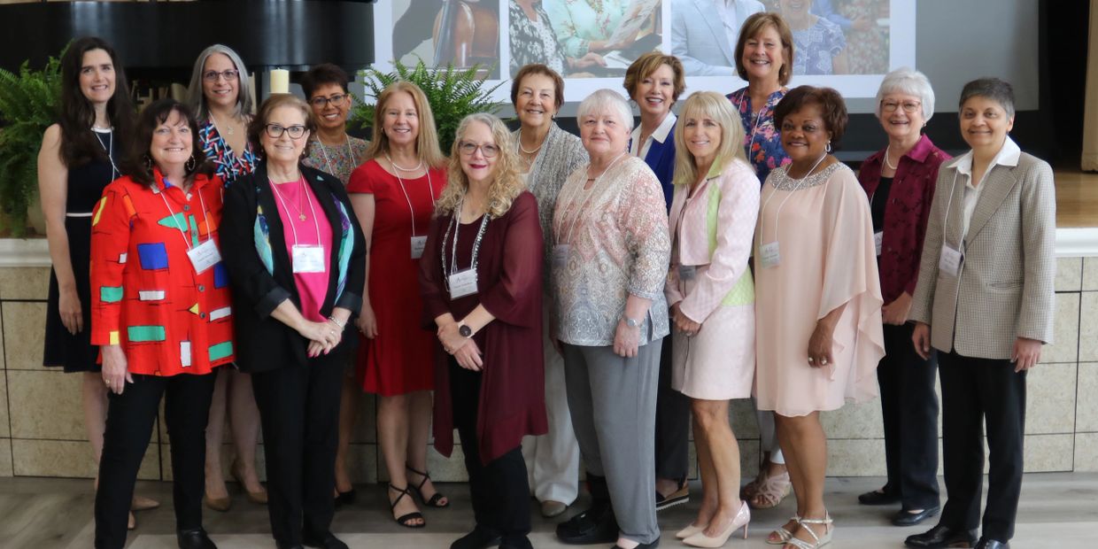Group of women dressed formally, posing indoors with name tags.