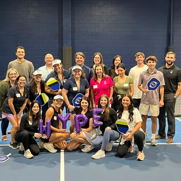 Group of people on a tennis court holding signs and balloons spelling 'HOPE'.