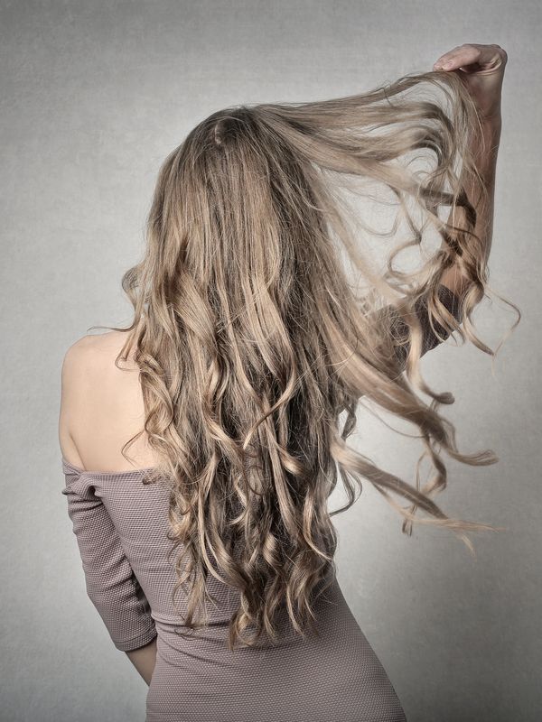 Woman with long med ash blonde hair with her back to you holding her hair out.
