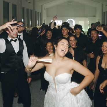Bride joyful at wedding reception surrounded by dancing guests.