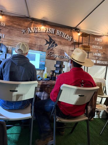 Two men sitting inside a tent booth with Angel Fish Builds signage.