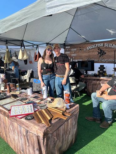 Couple standing at a market booth under a white tent.