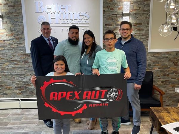 Group holding Apex Auto Repair banner indoors.