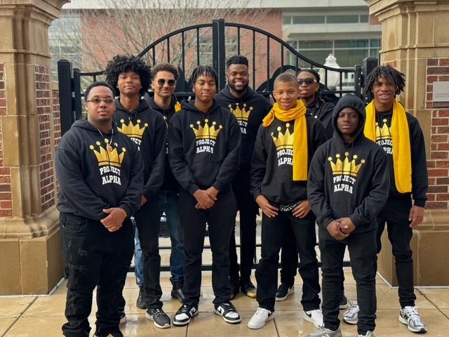 Group of young men wearing Project Alpha hoodies, standing together outdoors.