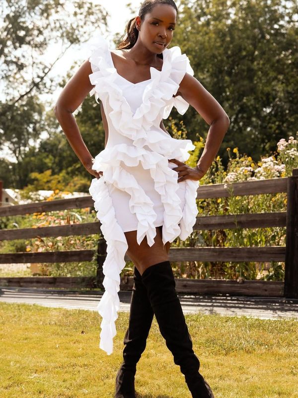 Woman posing outdoors in a white ruffled dress and black thigh-high boots.