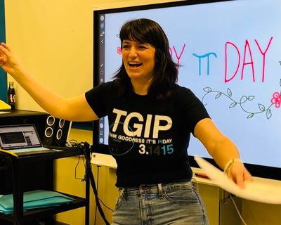 Maeve Siu singing to her students. Happy Pi Day is written on the board behind her. 