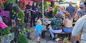 Outdoor gathering with live music and people enjoying a sunny day.