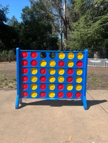 Outdoor Connect Four game set on a patio with trees in the background.