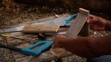 Manos trabajando con madera y sierra en un taller.