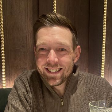 Smiling man in a brown sweater sitting at a table.