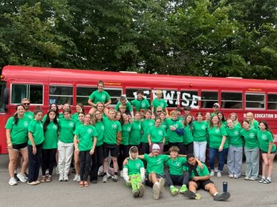 Group of people in green shirts posing in front of red bus.