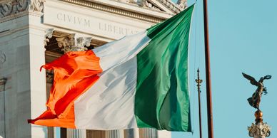 Irish flag flying with a traditional building behind and blue skies