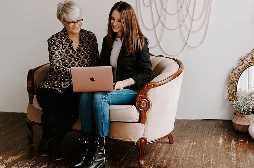Photo of two women sitting on a couch looking at a laptop