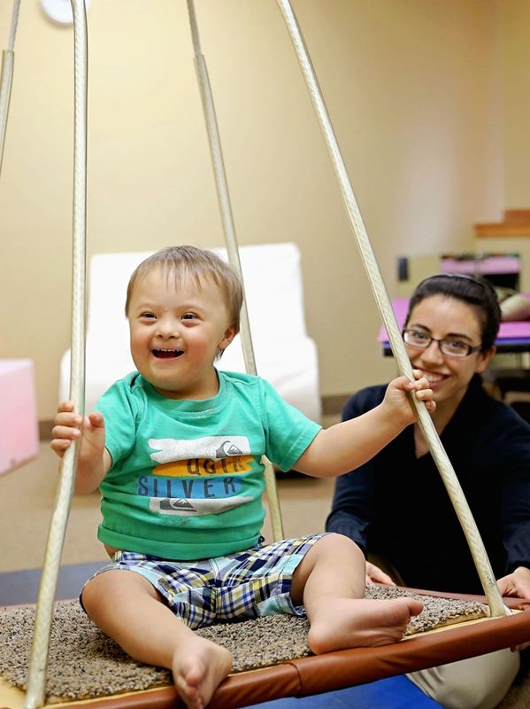 Therapist swinging child on a swing. Physical therapy. Physical therapist.