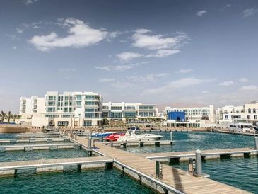 Modern marina with boats docked and white buildings in the background under a clear sky.