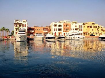 Luxury yachts docked by colorful waterfront buildings under a clear blue sky.