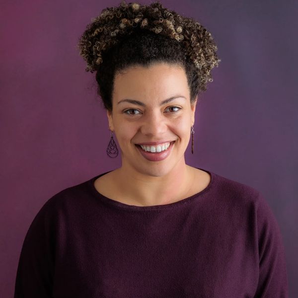 Behavior Analyst - Mixed woman with curly hair, wearing purple and smiling at the camera. 