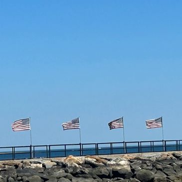 Four American flags flying on a pier against a clear blue sky.