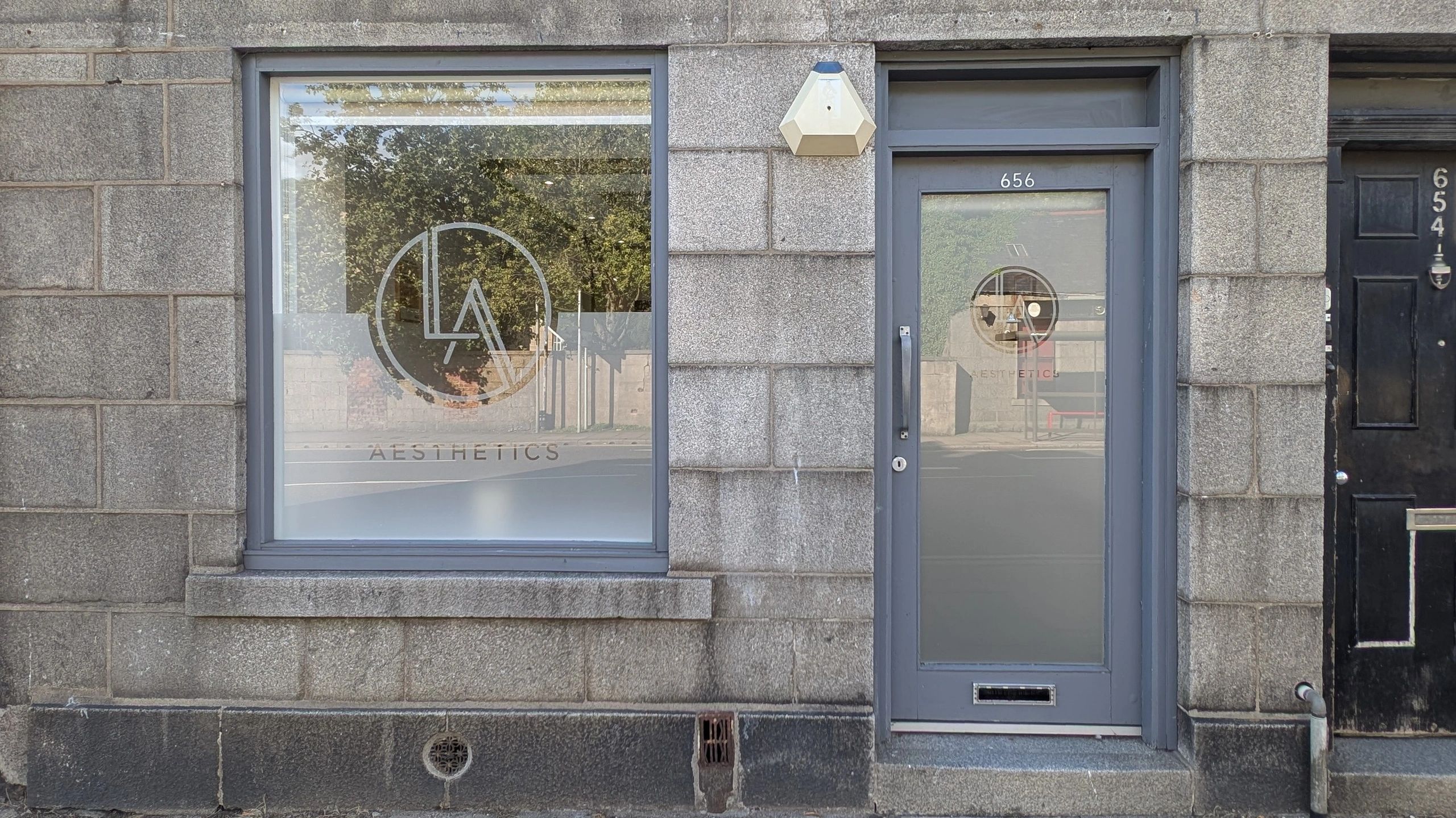 Stone building front with a door and window for an aesthetics business.