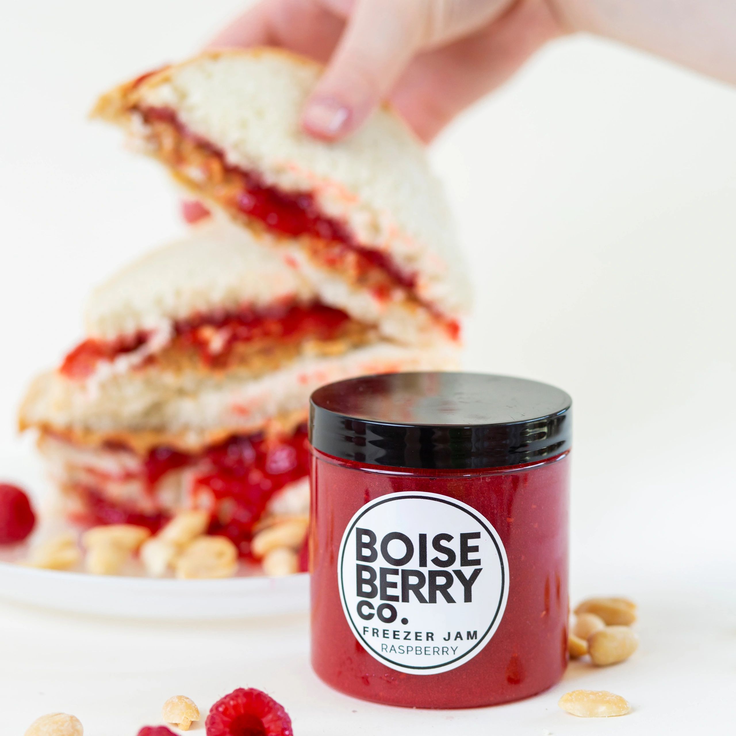 Jar of Boise Berry Co. raspberry freezer jam with sandwiches in the background.