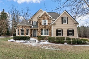 A large two-story house with stone and beige siding exterior and black shutters.