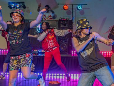 People dancing energetically on stage with colorful lights.