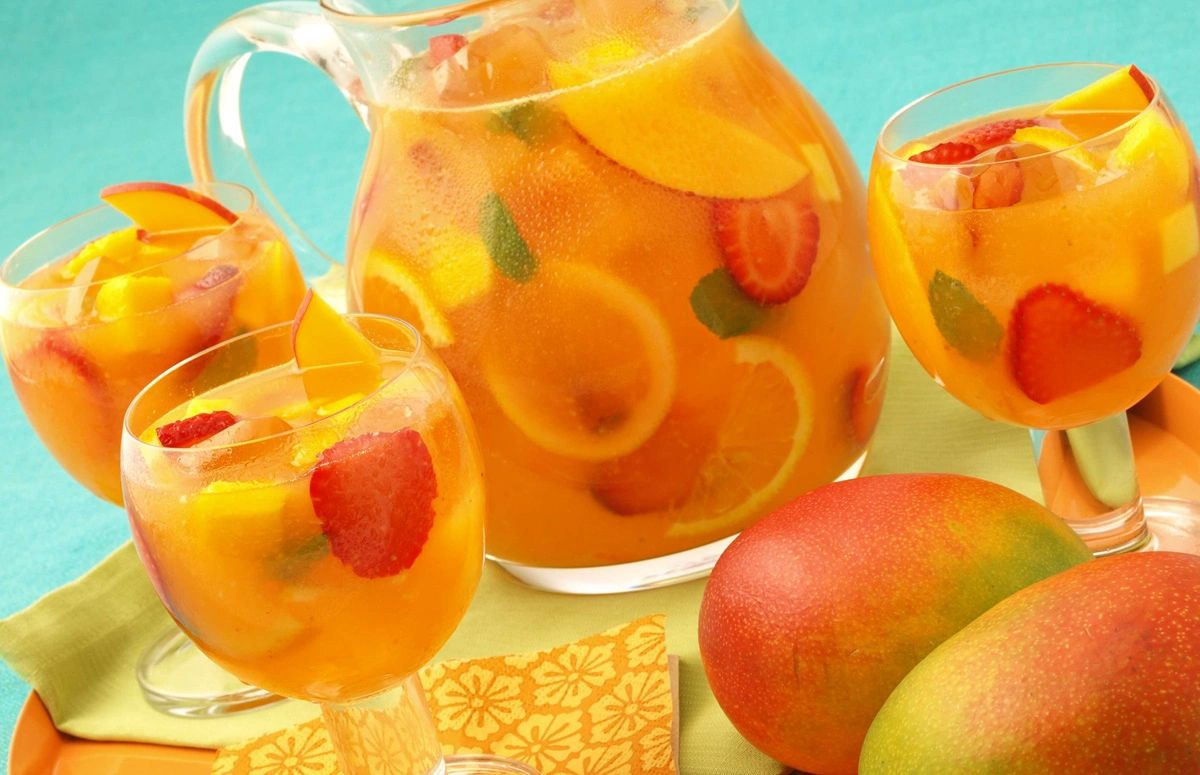 Refreshing fruit punch with mango, strawberry, and citrus slices in glasses and a pitcher.