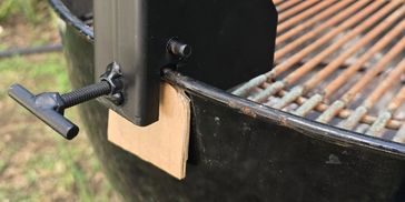Cardboard piece held by clamp on a barbecue grill.