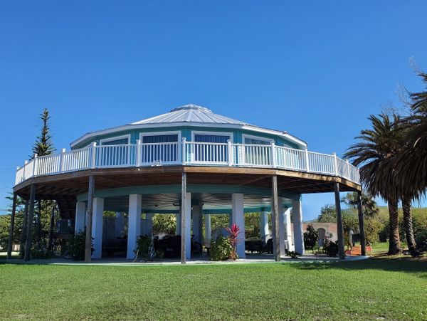 Round elevated house with white railings and blue siding under a clear sky.