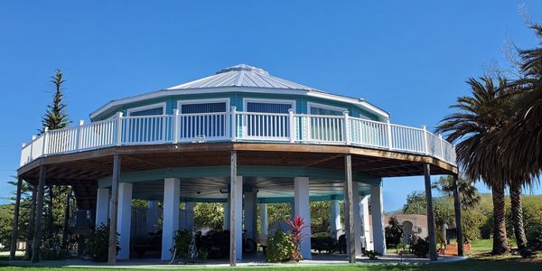 Elevated octagonal house with white railings under a clear blue sky.