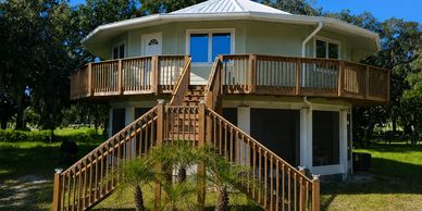 Elevated round Deltec home with a wooden deck and exterior stairs.